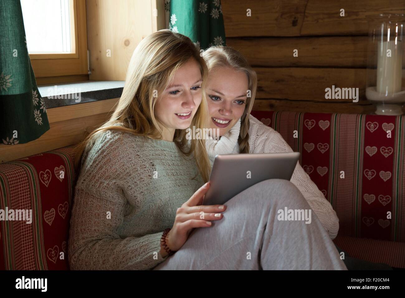 Two young women reading digital tablet in log cabin Stock Photo