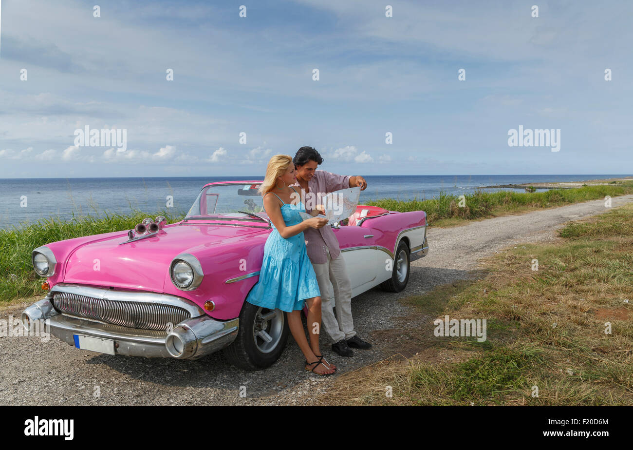 Young couple looking at map beside vintage convertible at coast, Havana, Cuba Stock Photo