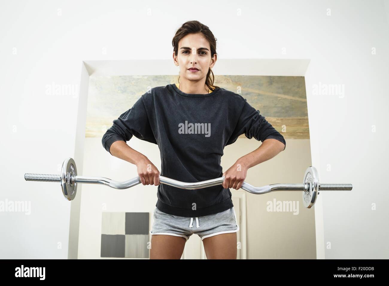 Young woman lifting barbell in living room Stock Photo