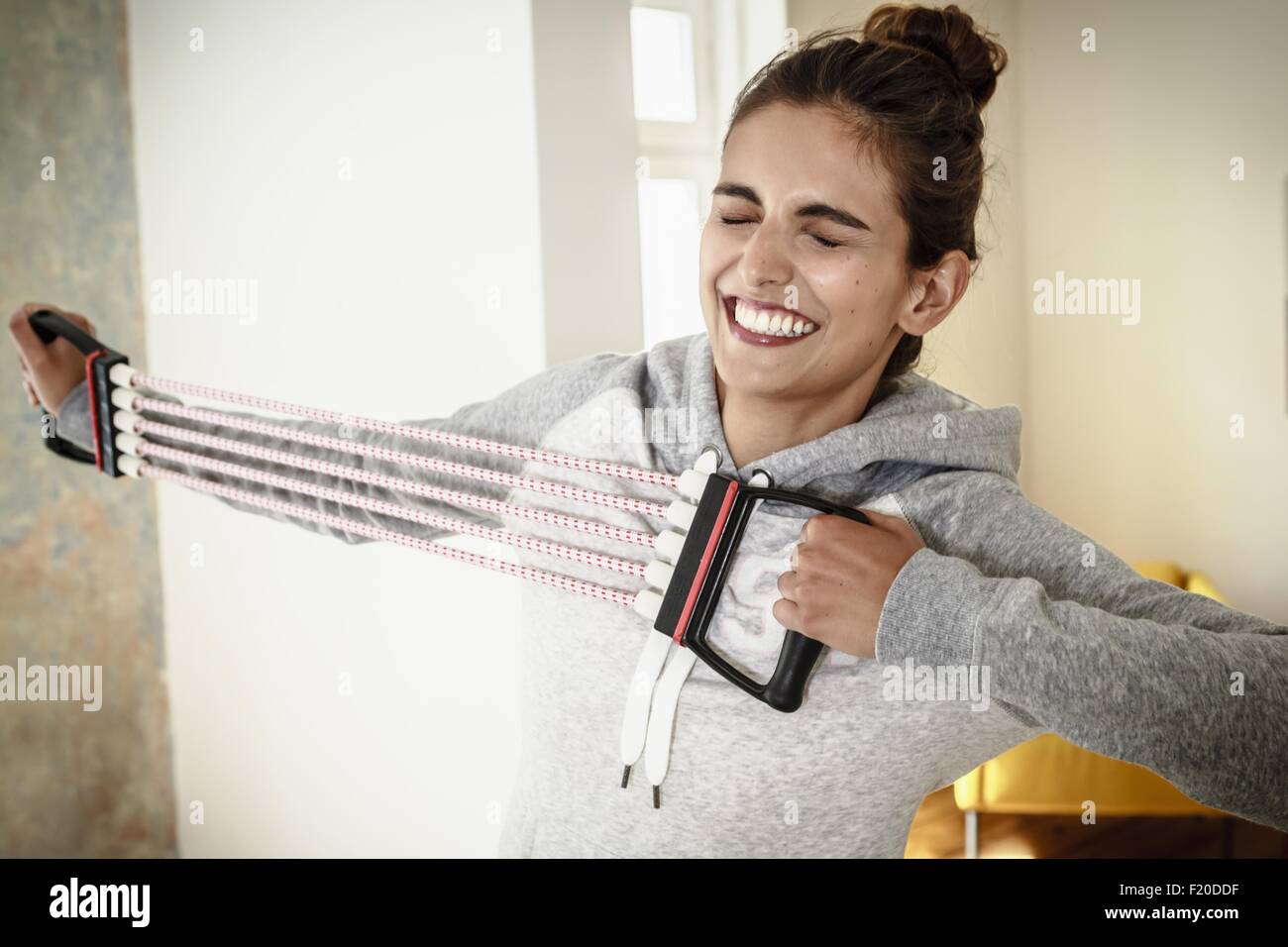 Young woman straining to exercise with chest expander in living room Stock Photo