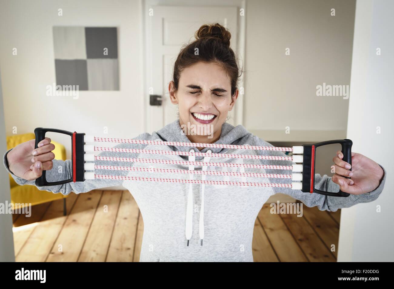 Young woman straining to exercise using chest expander in living room Stock Photo