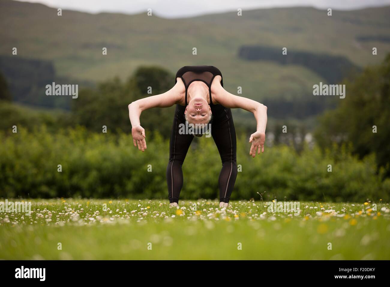Mature woman practicing yoga bending backward in field Stock Photo