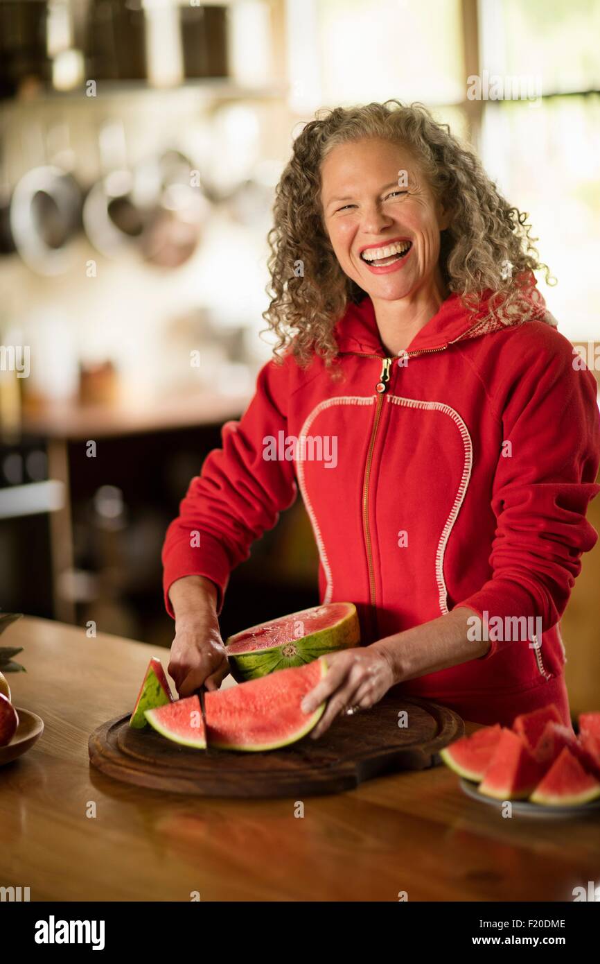 Portrait of mature woman slicing watermelon in kitchen Stock Photo