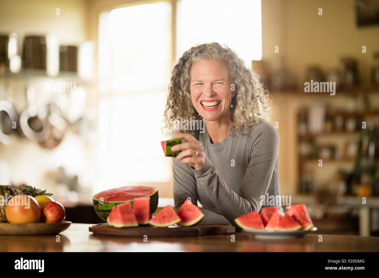 Portrait of mature woman eating watermelon in kitchen Stock Photo