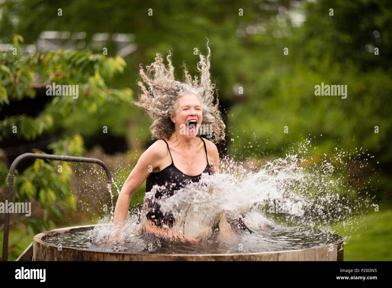 Mature woman splashing into fresh cold water tub at eco retreat Stock Photo
