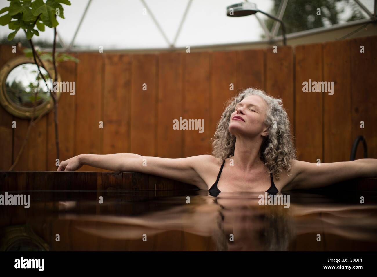 Mature woman relaxing in hot tub at eco retreat Stock Photo