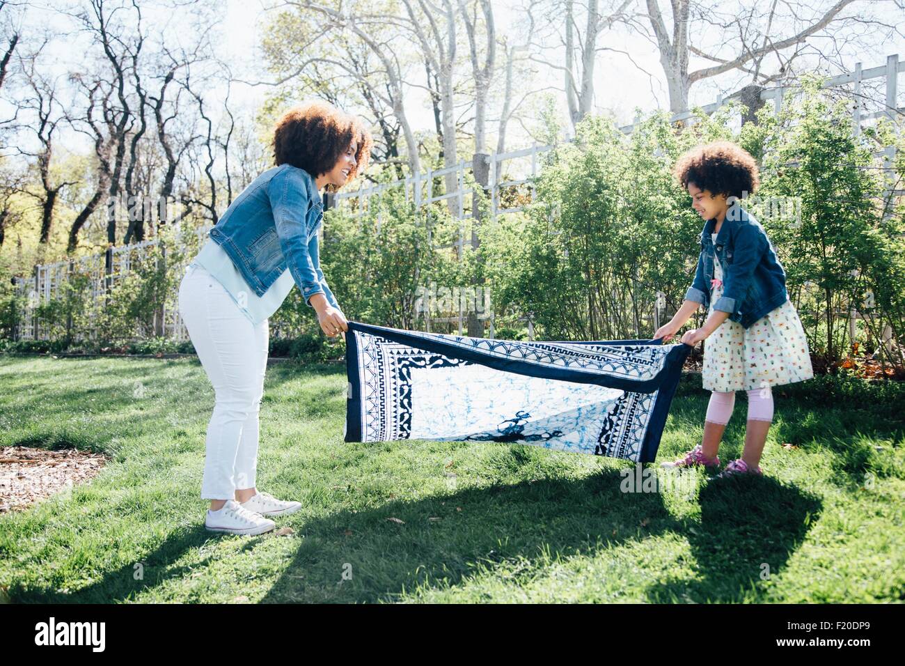 Side view of mother and daughter laying out blanket on grass Stock