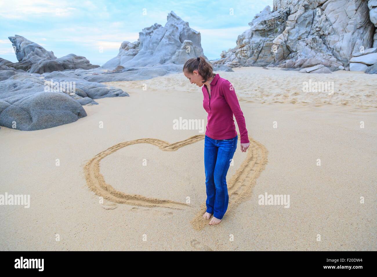 Mid adult woman on beach, drawing heart shape with feet Stock Photo