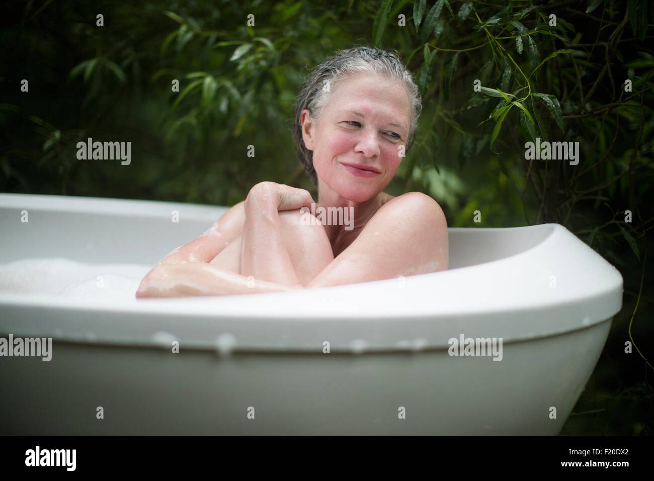Mature woman hugging knees in garden bubble bath at  eco retreat Stock Photo