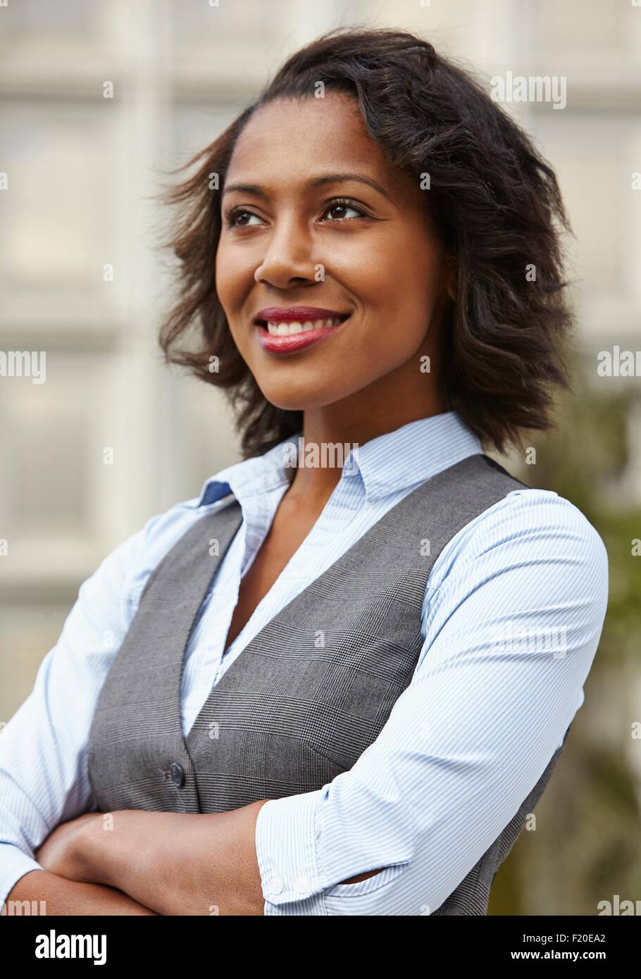 Portrait of young business woman, wearing waistcoat, looking away, arms folded, smiling Stock Photo