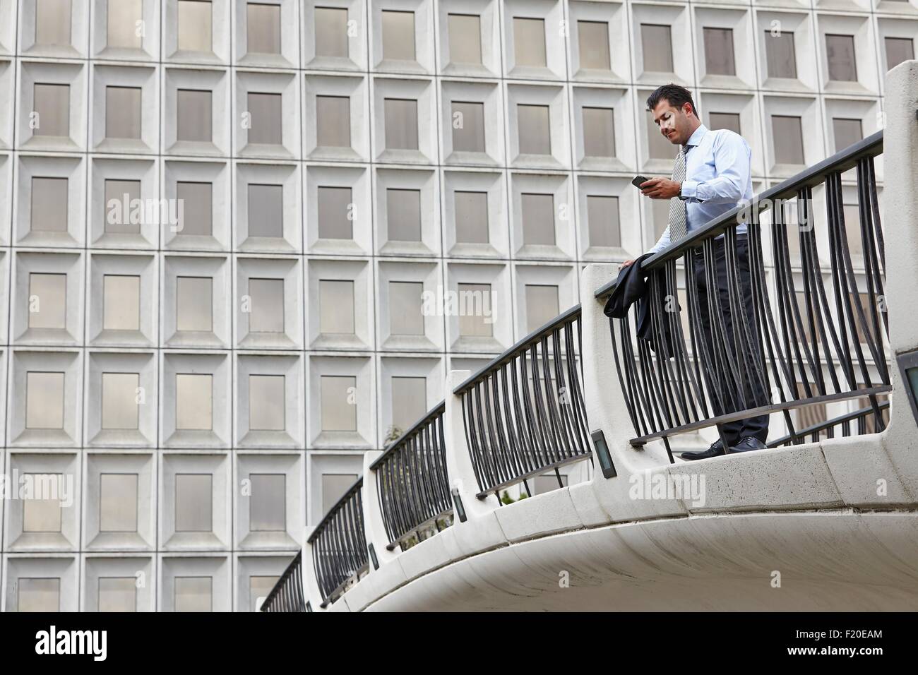 Mid adult business man standing on elevated walkway looking at smartphone Stock Photo