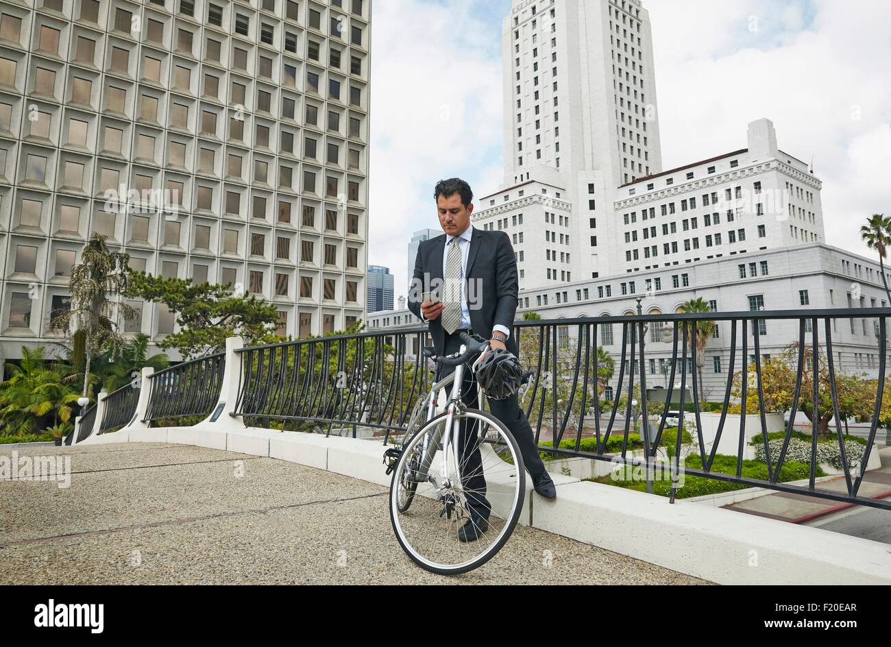 Business man on elevated walkway with bicycle looking at smartphone, Los Angeles City Hall, California, USA Stock Photo