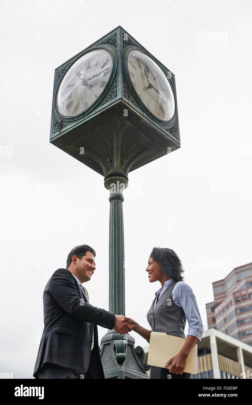 Low angle view side view of business people shaking hands underneath clock, waist up Stock Photo