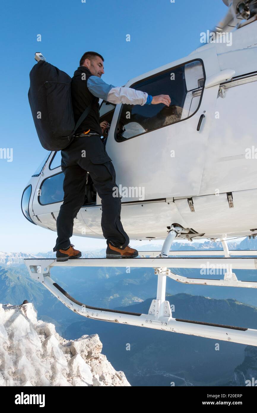 Male BASE jumper standing on side of helicopter preparing to land on summit, Dolomites, Italy Stock Photo