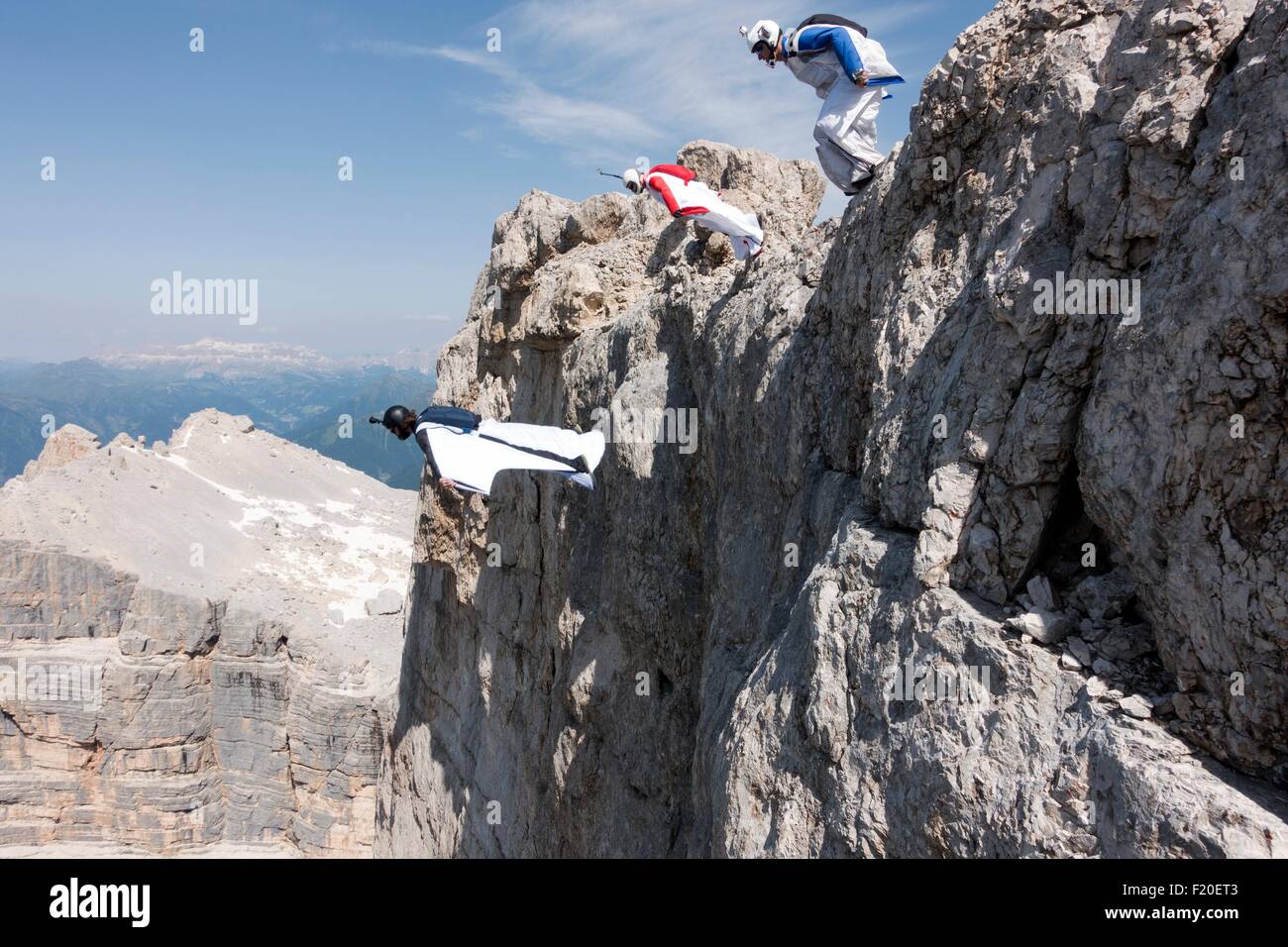 Three male BASE jumpers exiting from mountain top, Dolomites, Italy Stock Photo