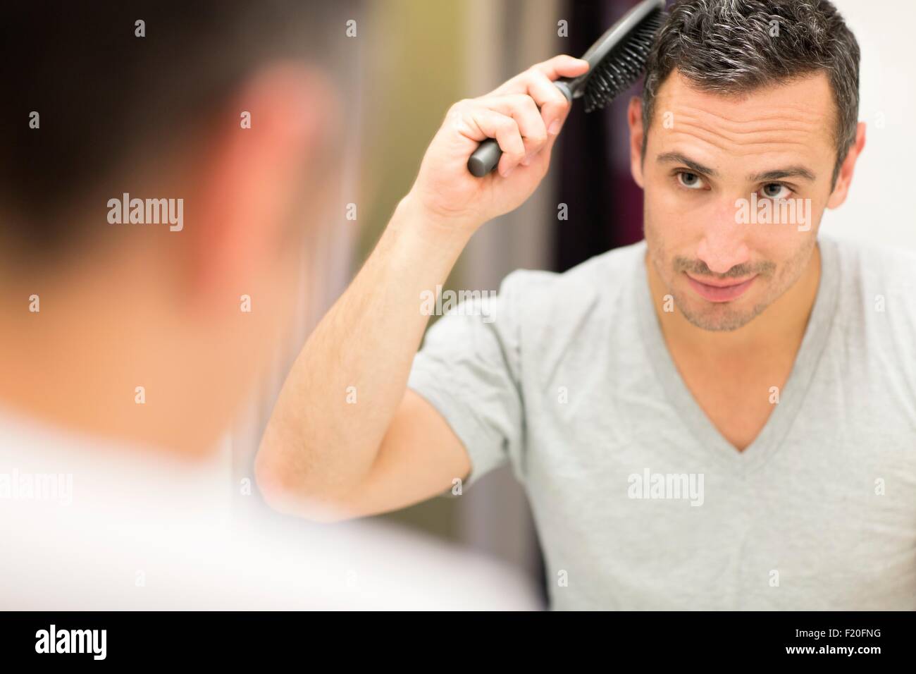 Mid adult man, looking in mirror, brushing hair Stock Photo