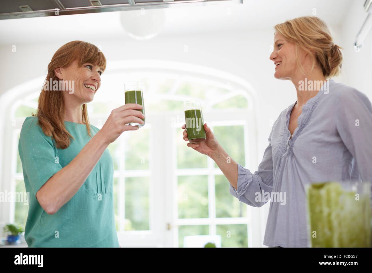 Women drinking green vegan smoothie in kitchen Stock Photo