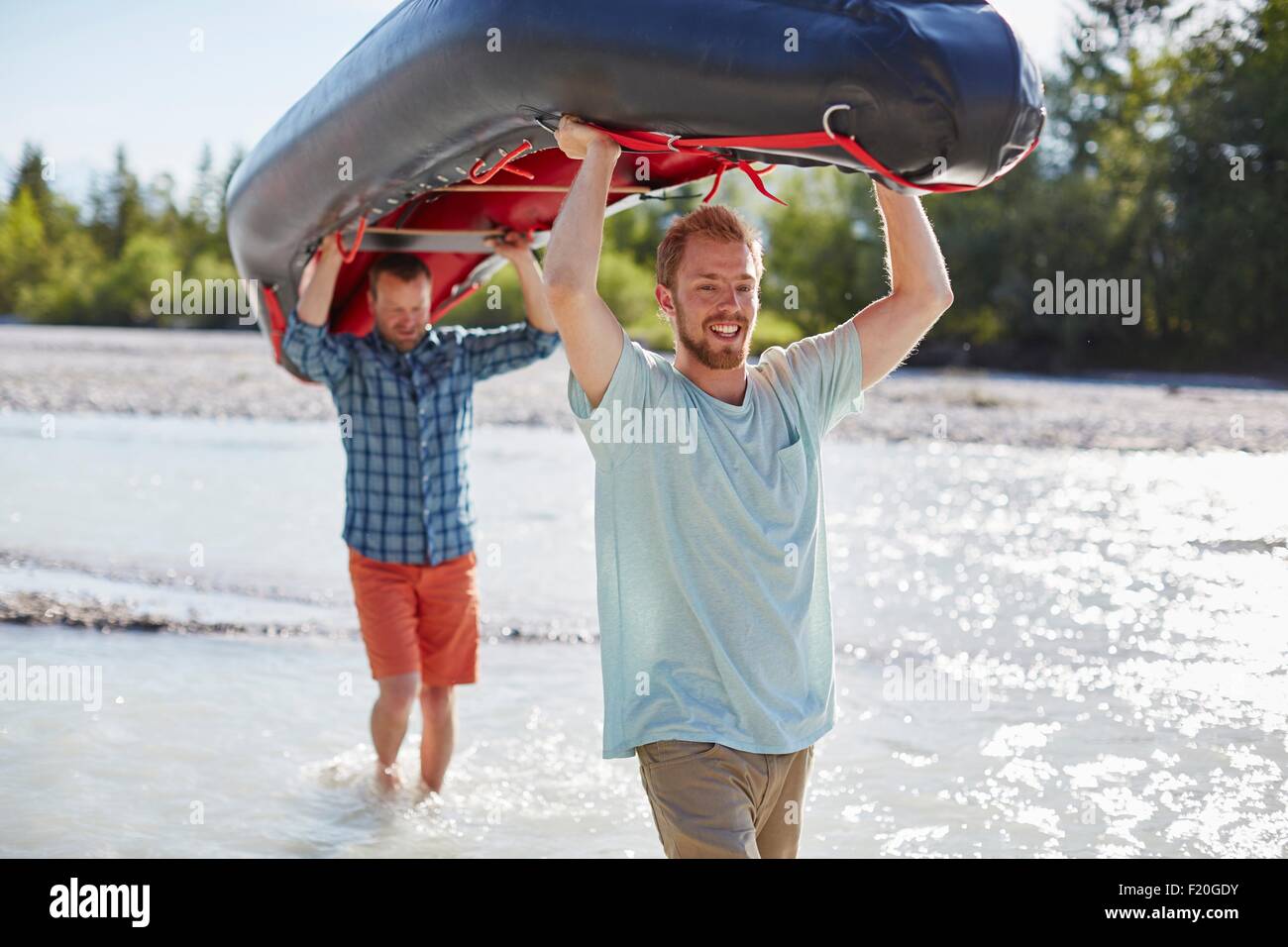 Two men carrying dinghy above their heads through shallow water Stock Photo