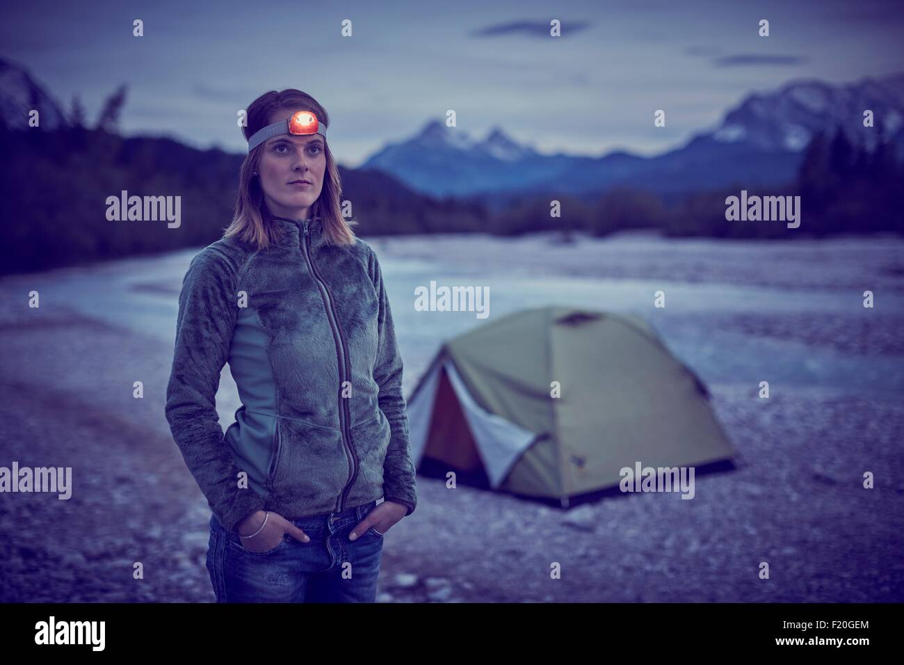 Young woman wearing headlamp, hands in pockets, looking away, Wallgau, Bavaria, Germany Stock Photo