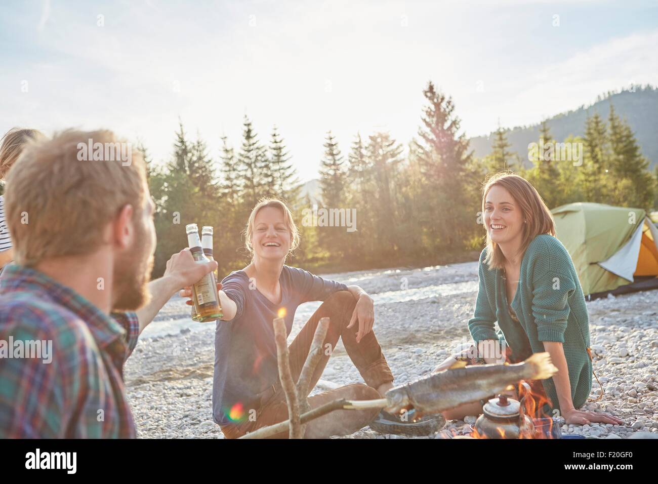 Adults sitting around campfire making a toast with beer bottles Stock Photo