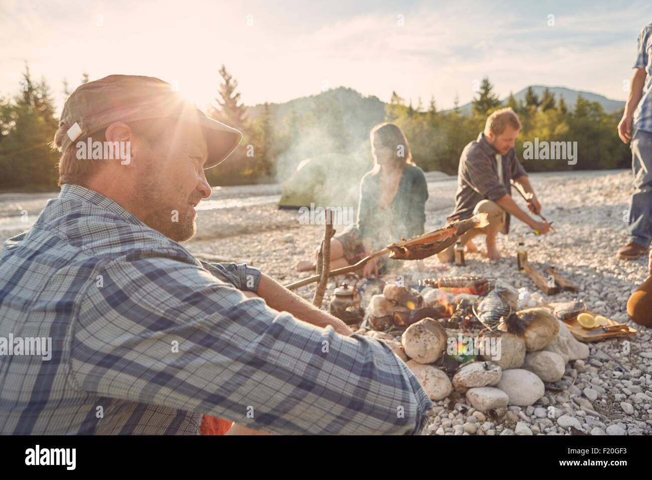 Side view of mature adult man sitting next to campfire, looking away Stock Photo