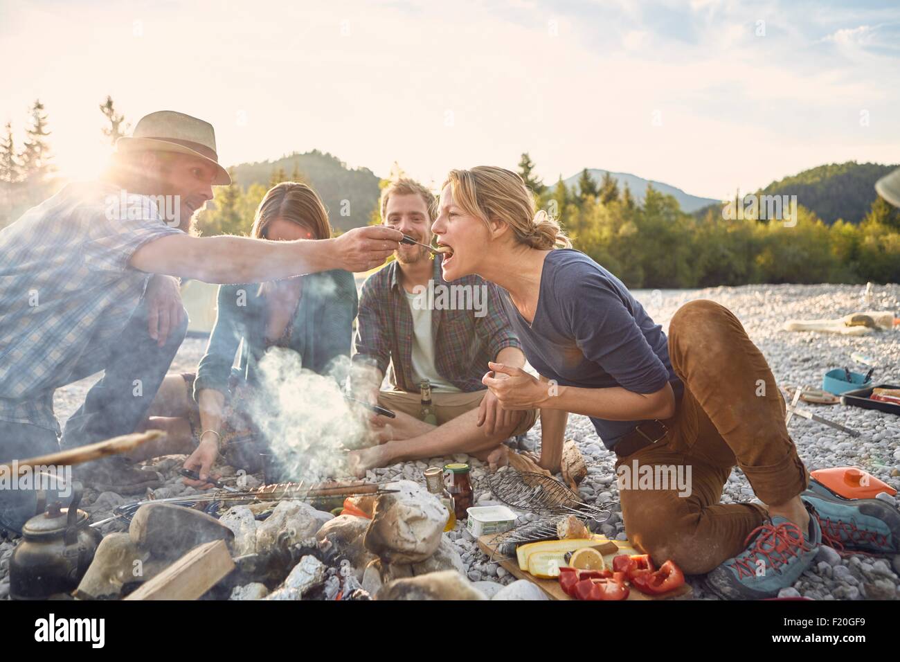 Mid adult man feeding mature woman across a campfire Stock Photo