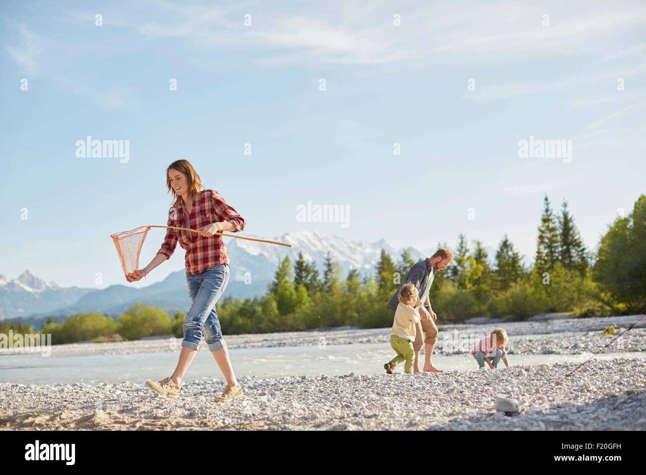 Young woman carrying fishing net by river, people in the background, Wallgau, Bavaria, Germany Stock Photo