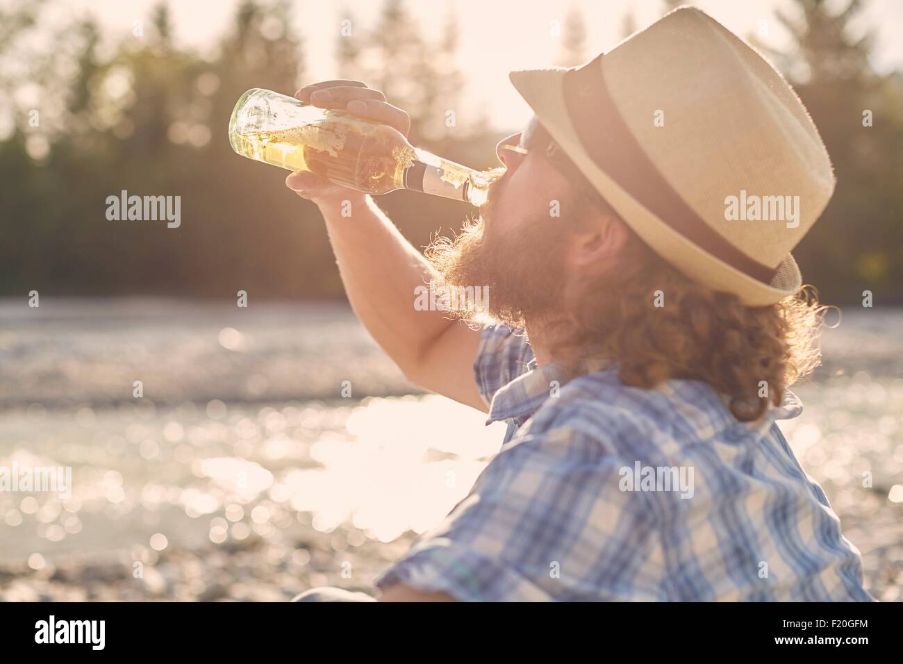 Side view of mid adult man wearing hat drinking beer from beer bottle Stock Photo