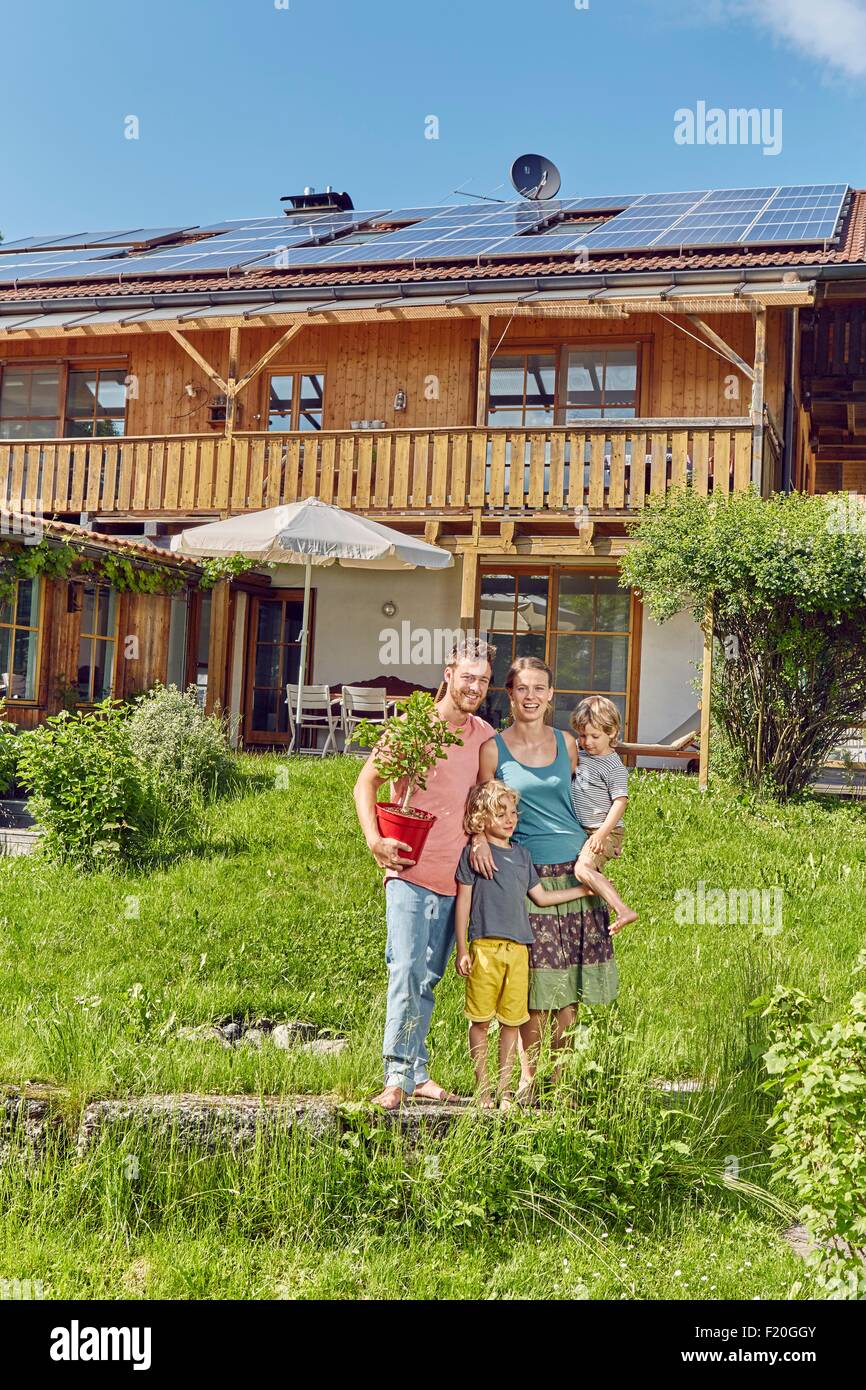 Portrait of young family, holding pot plant, standing in front of house with solar panelled roof Stock Photo