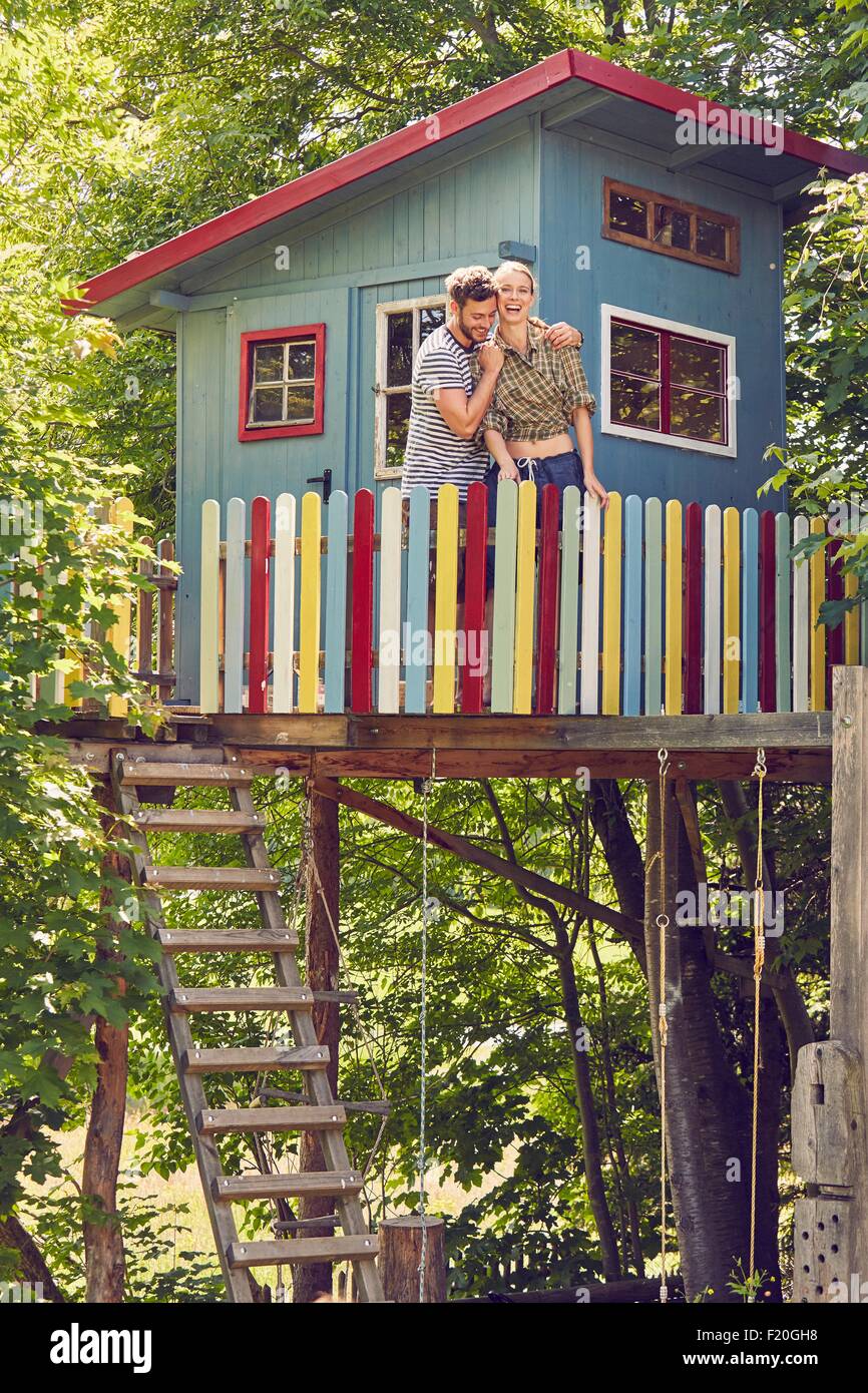 Young couple standing in tree house, hugging, laughing Stock Photo