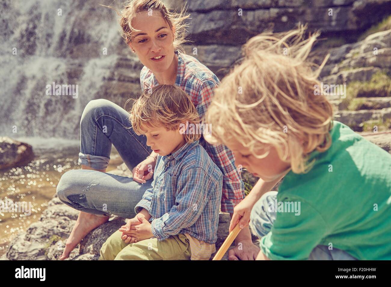 Mother and sons, sitting on rocks by waterfall Stock Photo