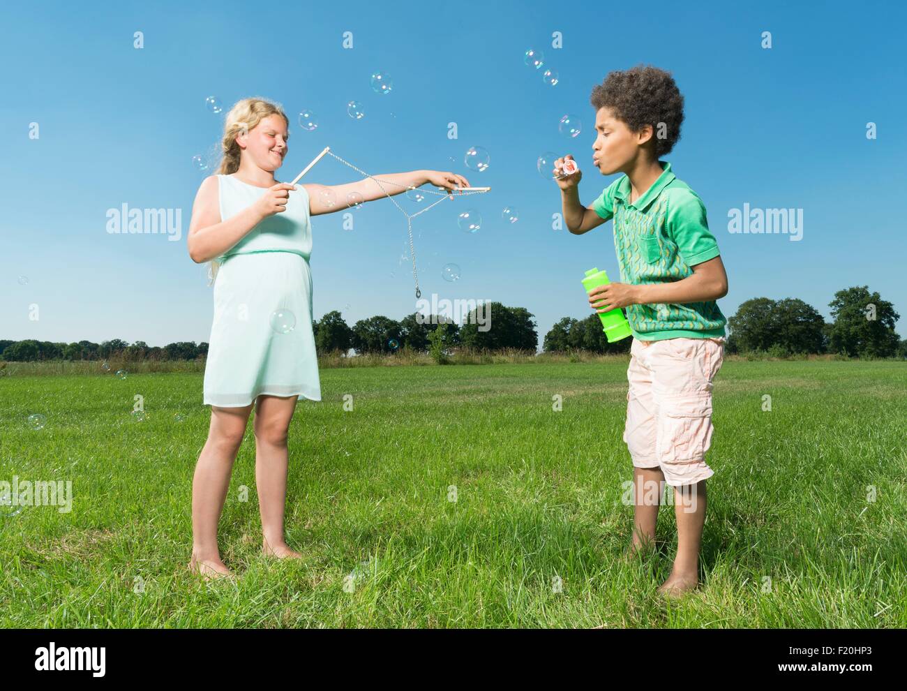 Girl and boy blowing bubbles in field Stock Photo