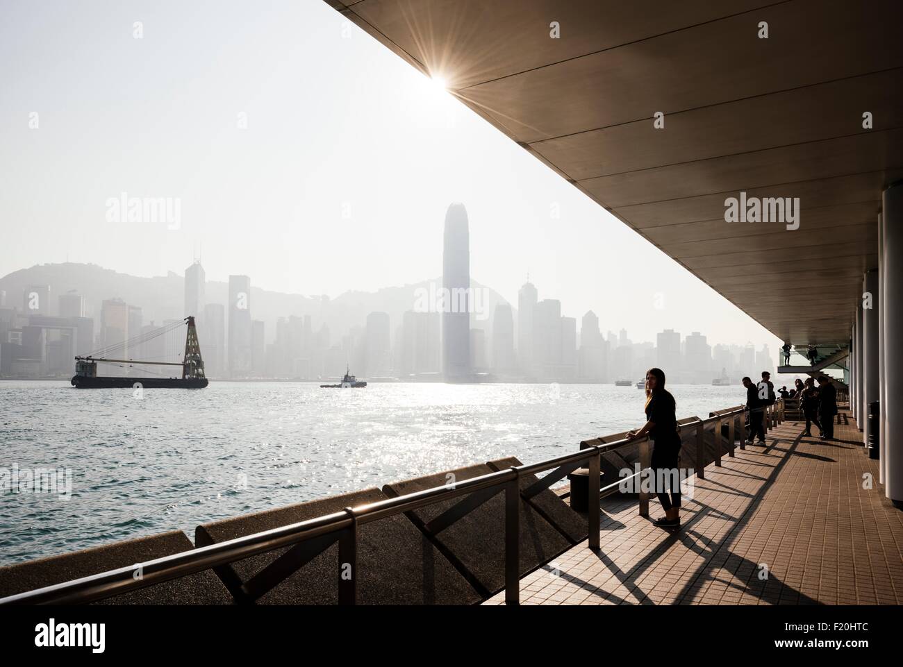 Silhouetted side view of young woman standing looking out over water at skyline, Hong Kong, China Stock Photo