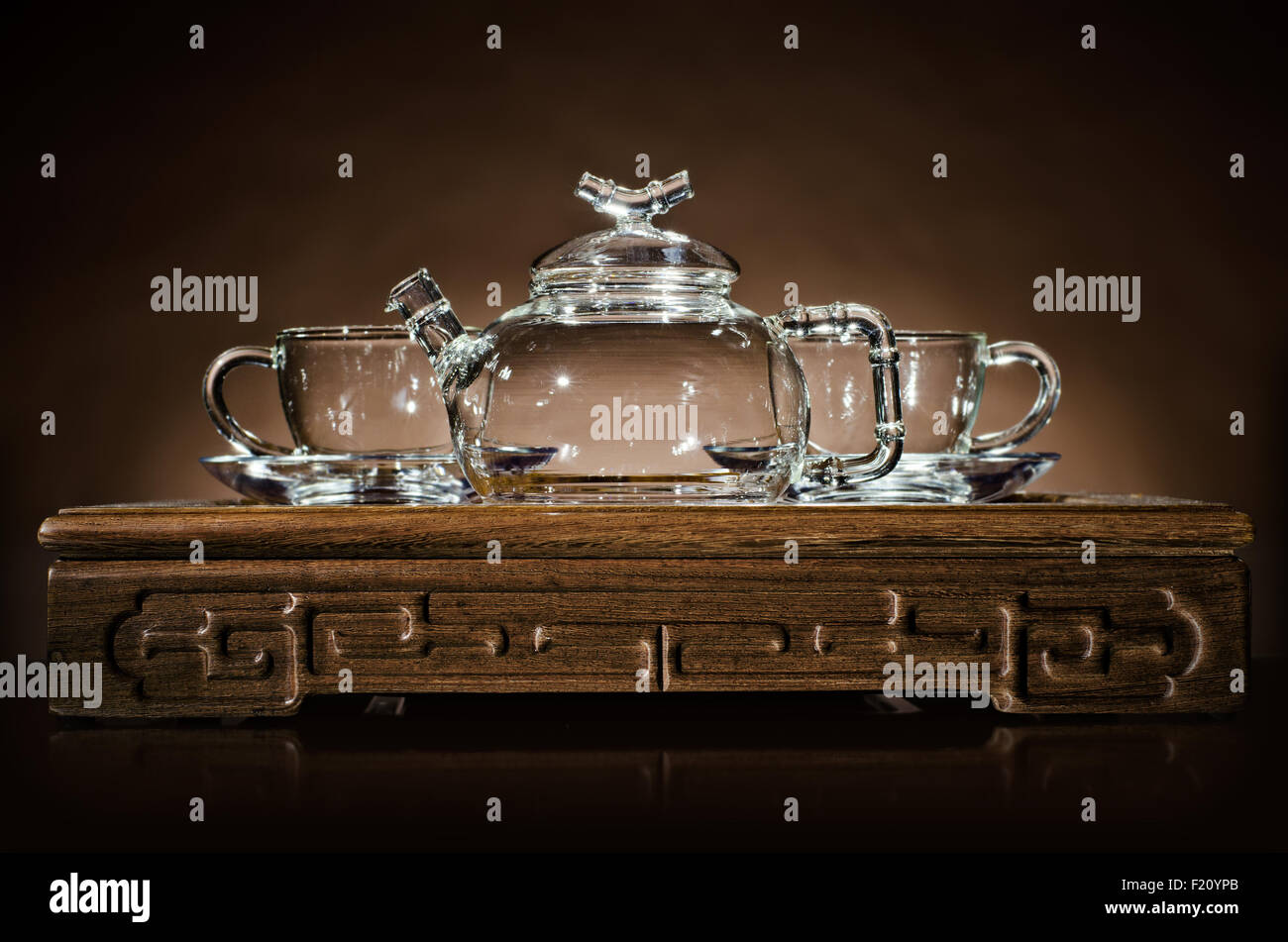 horizontal  photo  of the glass teapot with  cup on  wooden trivet, on dark background Stock Photo