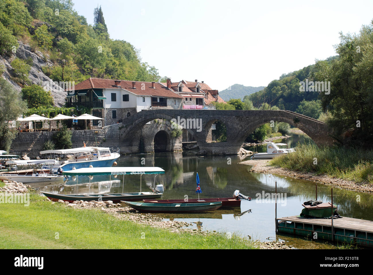 a medieval bridge crosses a small river with tour boats in the foreground and housing behind in Montenegro close to Cetinje Stock Photo
