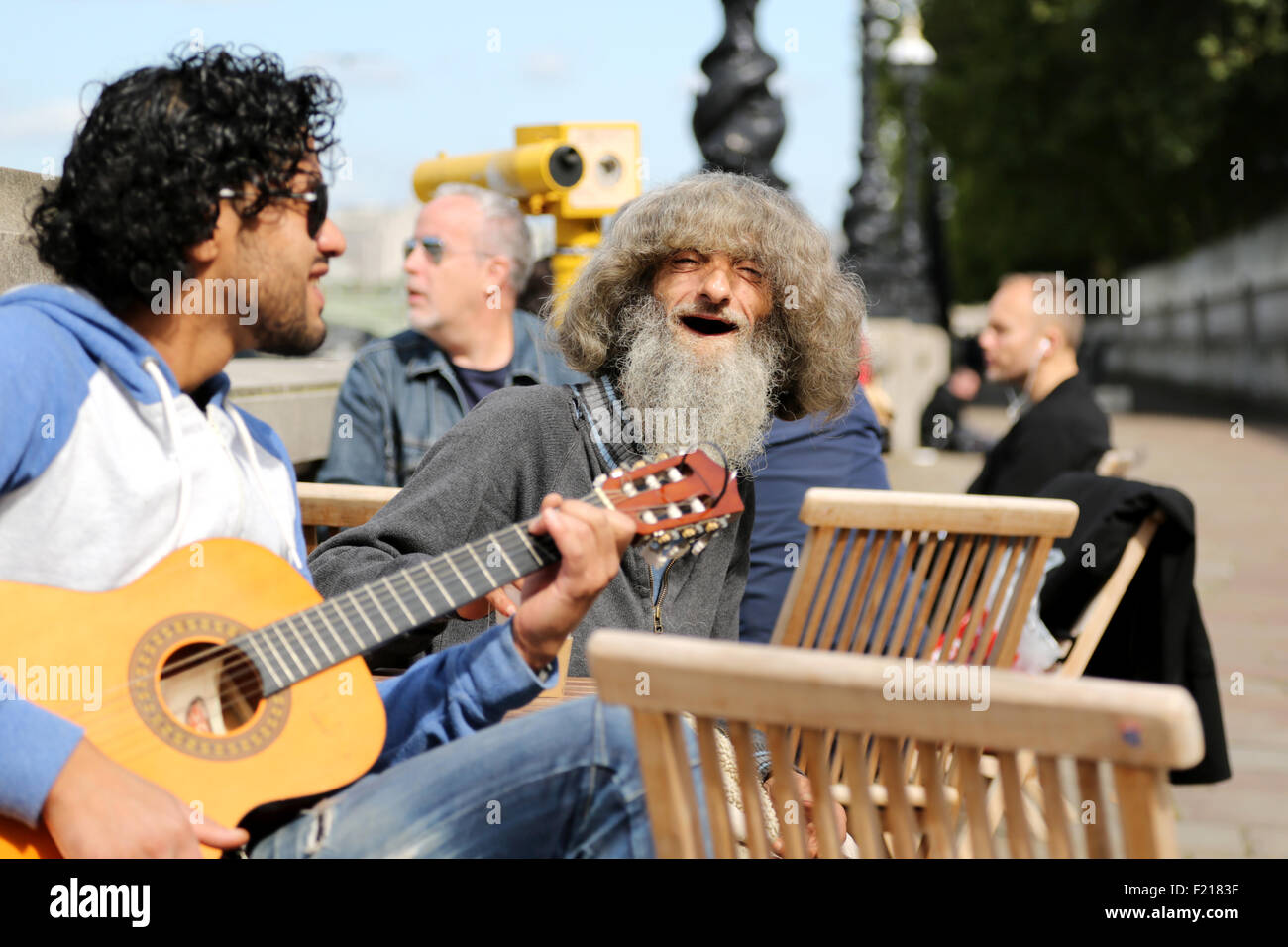 A busker playing an acoustic guitar entertains customers outside a coffee takeaway stall on londons southbank on a sunday morning. One eccentric guy. Stock Photo