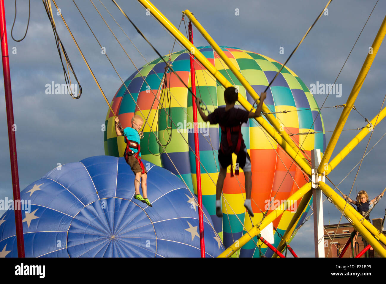 Hot air balloons launch as children play on bungees in the foreground.  Summer festival in Lewiston, Maine USA. Stock Photo