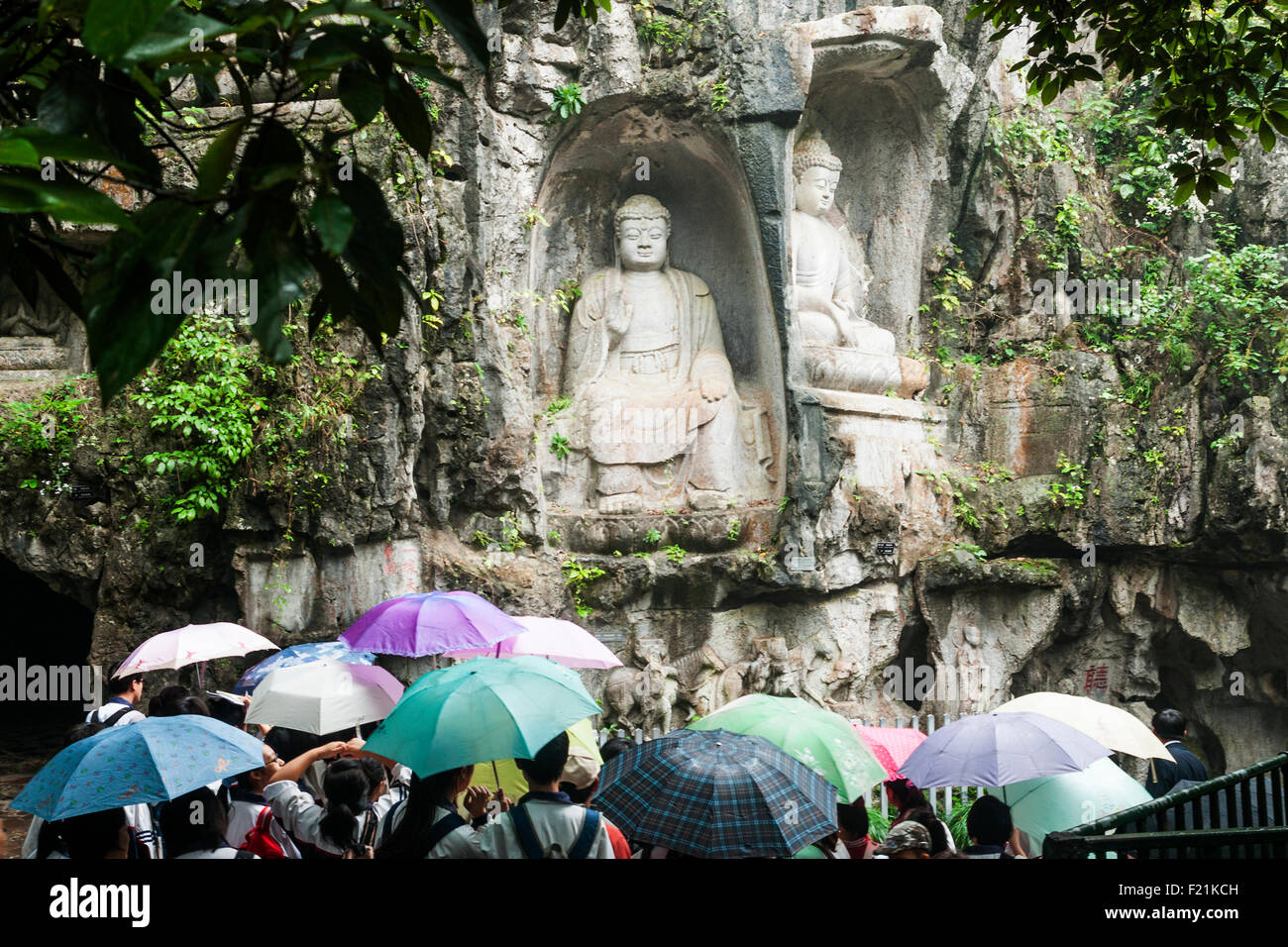 Tourists with umbrellas visiting Buddhas carved into rock face of Feilai Feng hill at Lingyin Temple Stock Photo