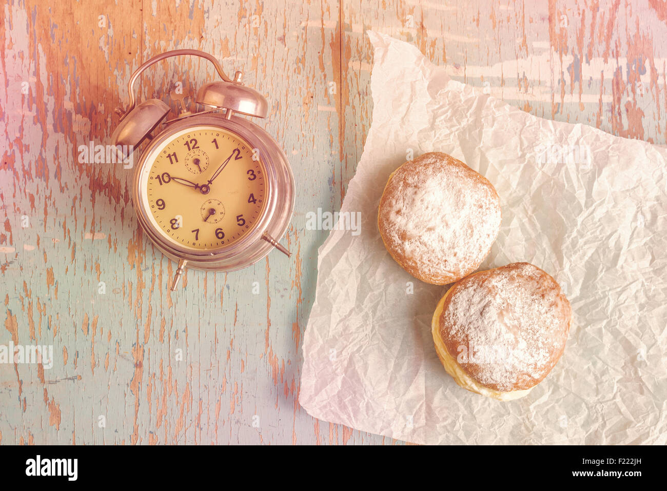 Sweet sugary donuts and vintage alarm clock on rustic wooden kitchen table, top view of tasty bakery doughnuts Stock Photo