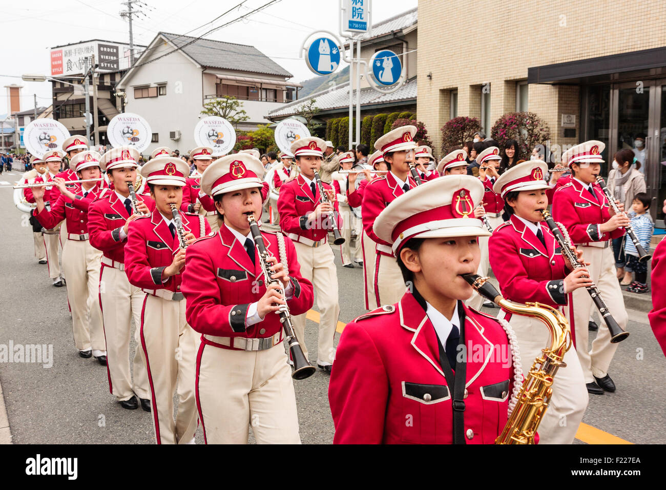 Genji Festival parade in Japan. Women's brass band marching at head of parade. Band members dressed in white and pink military style uniforms. Stock Photo