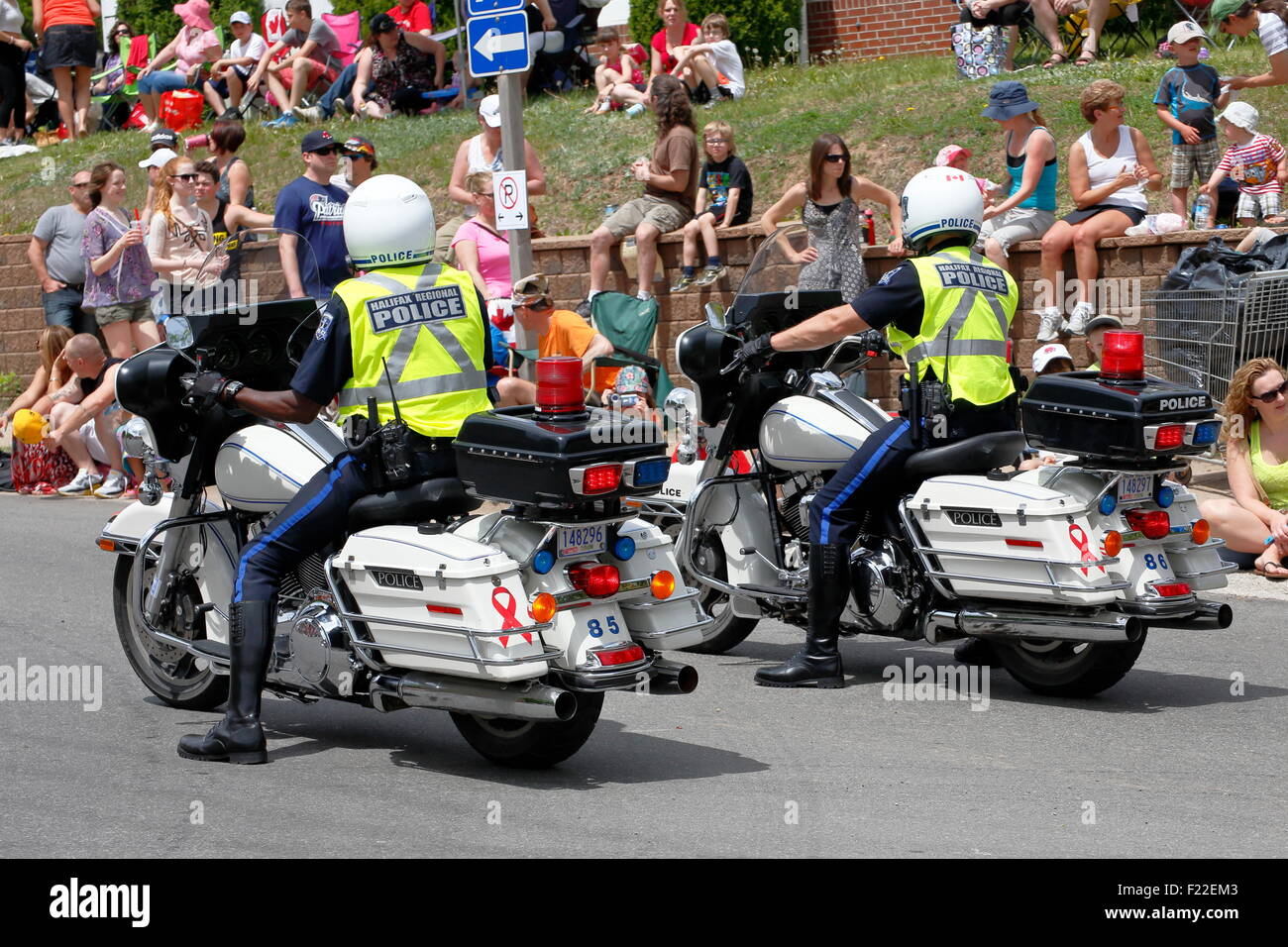 Two policemen one black and one white on police motorcycles beside a crowd of people enforcing the law and watching Stock Photo