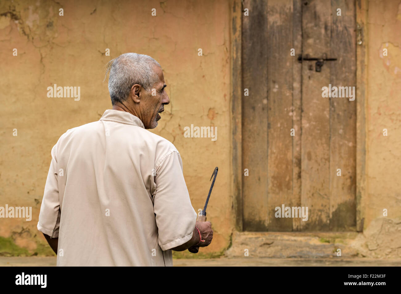 a candid portrait of a middle-aged Nepalese farmer man with a large pruning knife against a old wall and door background Stock Photo