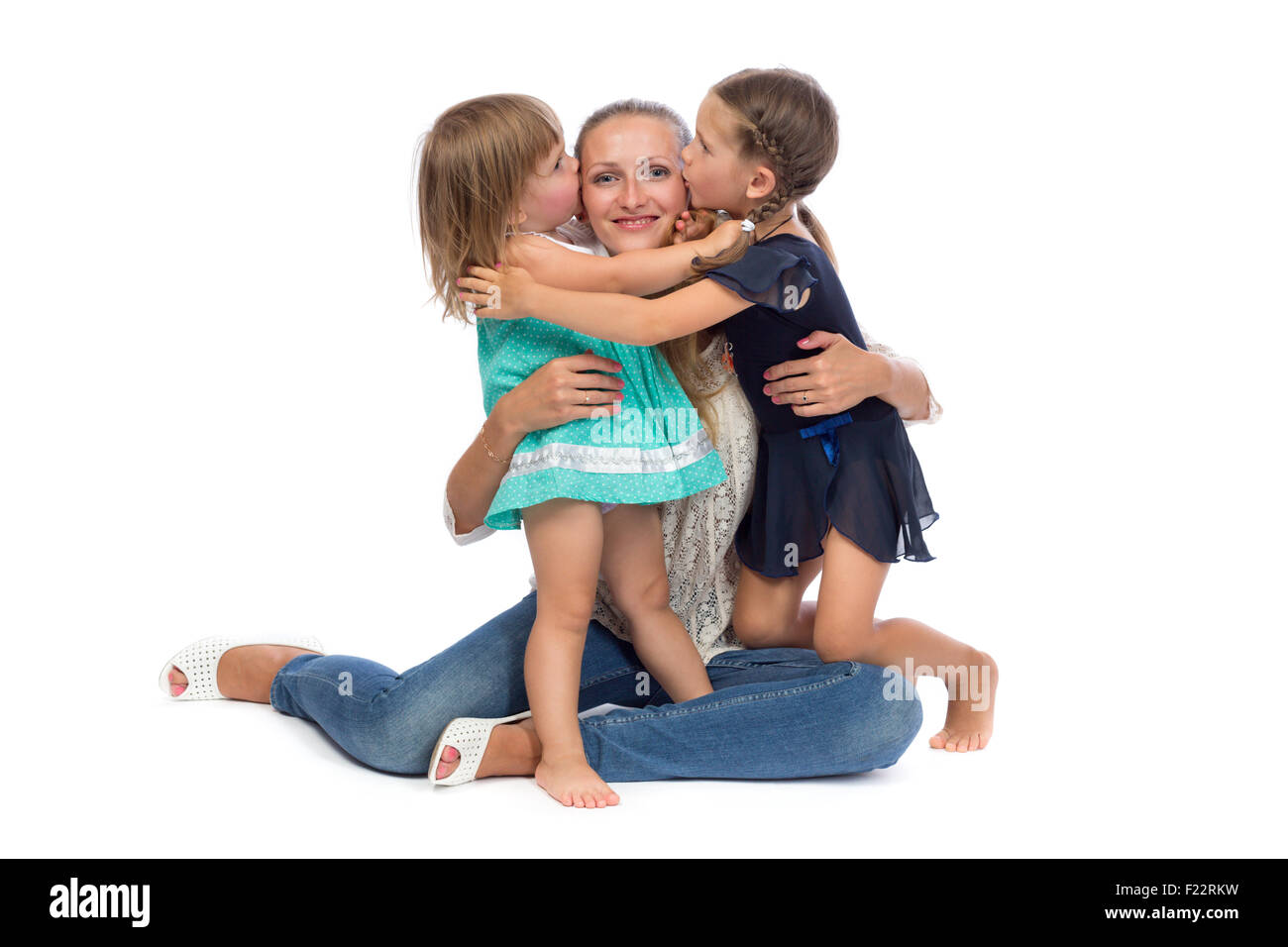 Two little daughters kiss Mom in the studio on a white background. Stock Photo