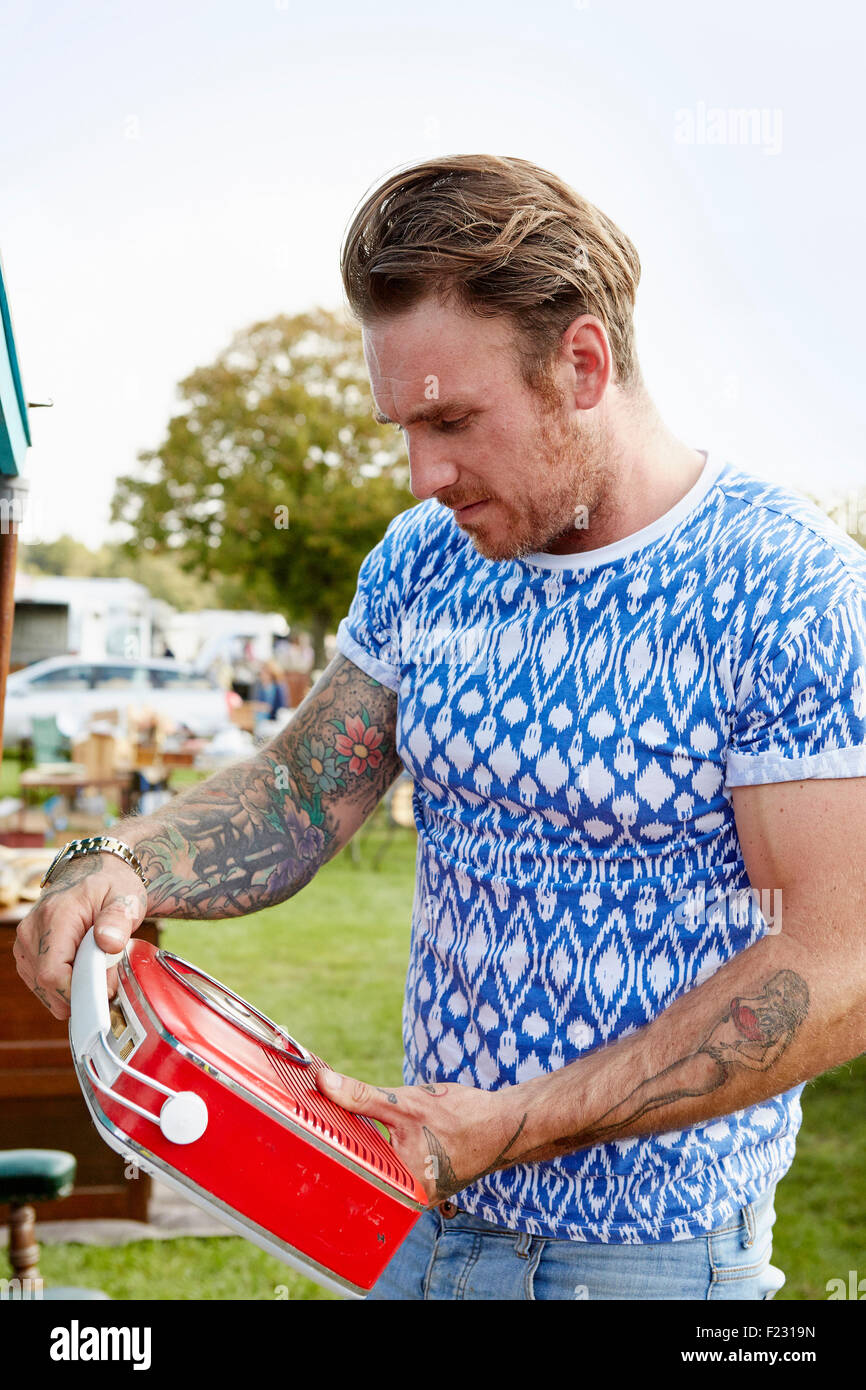Man with tattoos looking at a red vintage radio at a flea market. Stock Photo