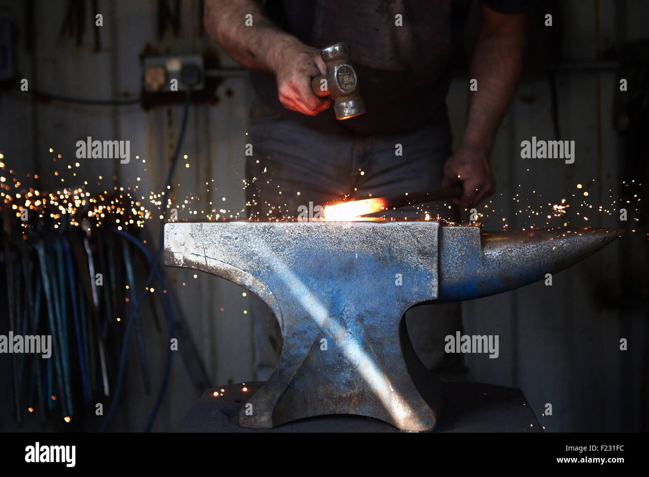 A blacksmith shaping a hot piece of iron on an anvil with a hammer, with sparks flying. Stock Photo