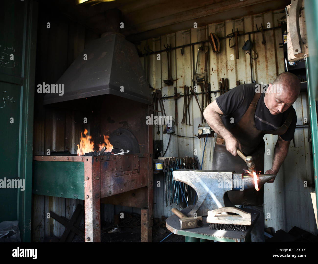 Blacksmith shaping a hot piece of iron on an anvil in a traditional forge with an open fire. Stock Photo