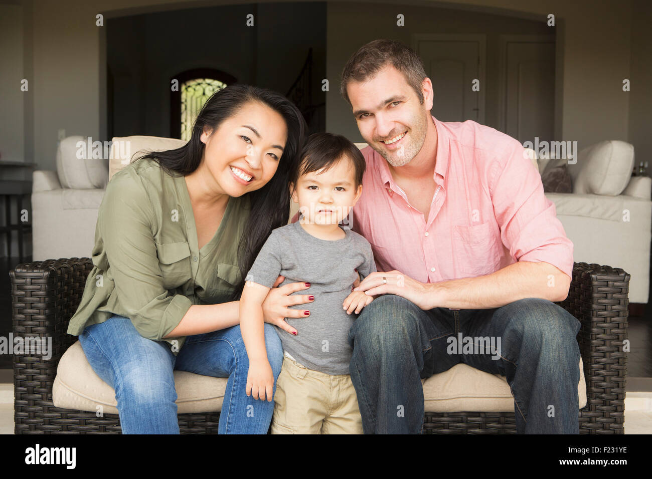 Smiling man and woman sitting side by side on a sofa, posing for a picture with their young son. Stock Photo