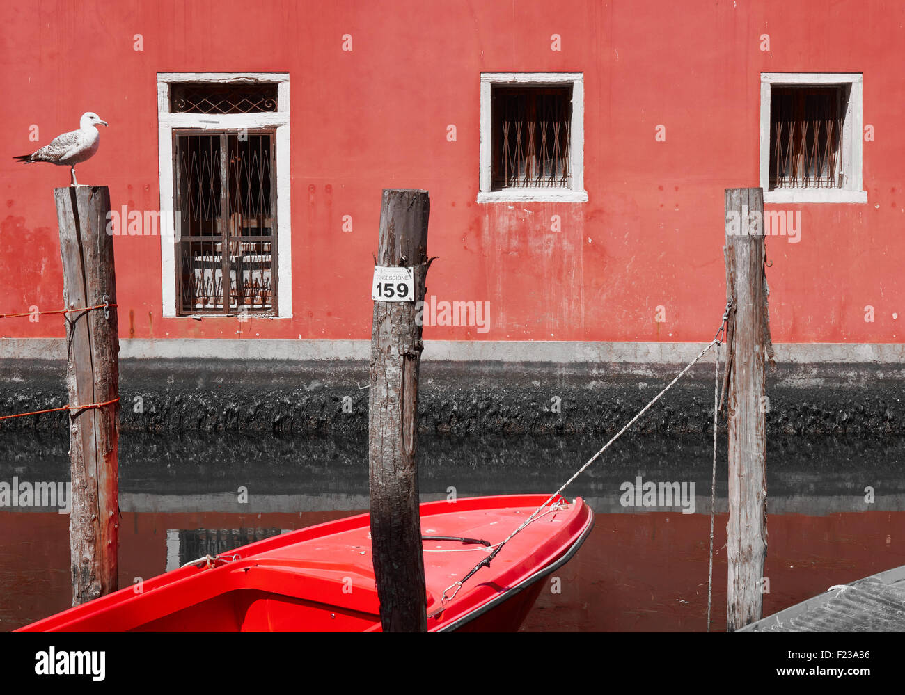 Canalside scene with wooden mooring poles (palina) seagull and small red boat Chioggia Venetian Lagoon Veneto Italy Europe Stock Photo