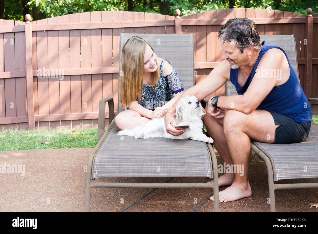 Caucasian father in 50s and blond teenage daughter laugh at something on an iphone as they sit outdoors with their dog Stock Photo