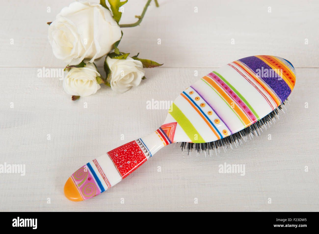 A brightly coloured hairbrush on a white background with two white roses flowers Stock Photo